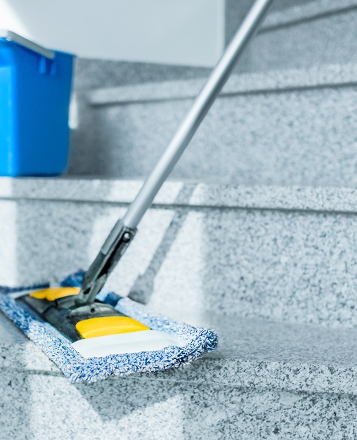 Nettoyage d'escalier en granit avec serpillière microfibre Mise au point sur une serpillière microfibre bleue et blanche nettoyant une marche d'escalier en granit moucheté, un seau bleu est visible en arrière-plan.